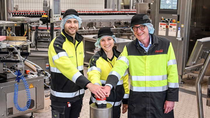 Zahlreiche Gäste wie Bürgermeister Guido Orthen (rechts) nahmen an der feierlichen Inbetriebnahme der modernisierten PET-Mehrweglinie am Coca-Cola Standort in Bad Neuenahr-Ahrweiler teil. Außerdem auf dem Bild links Hannes Bessinger (Betriebsleiter) und mittig Helen Schönknecht (Projektleiterin). (Bild: Coca-Cola)
